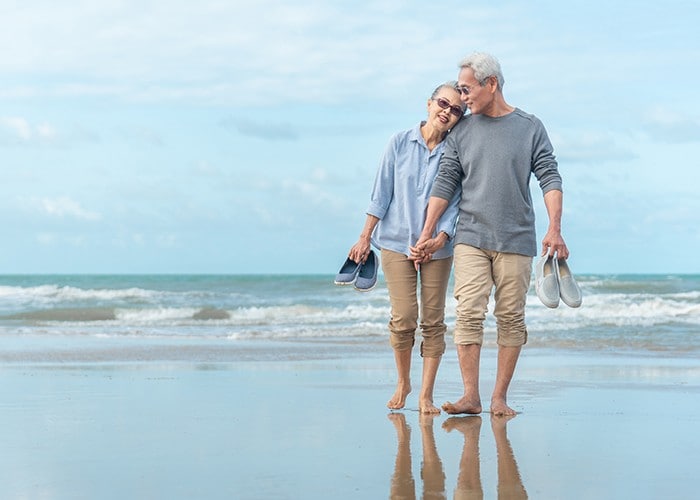 Happy senior couple holding hands and walking on beach.