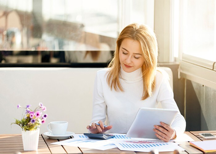 A woman sitting at a table with her coffee calculating her finances